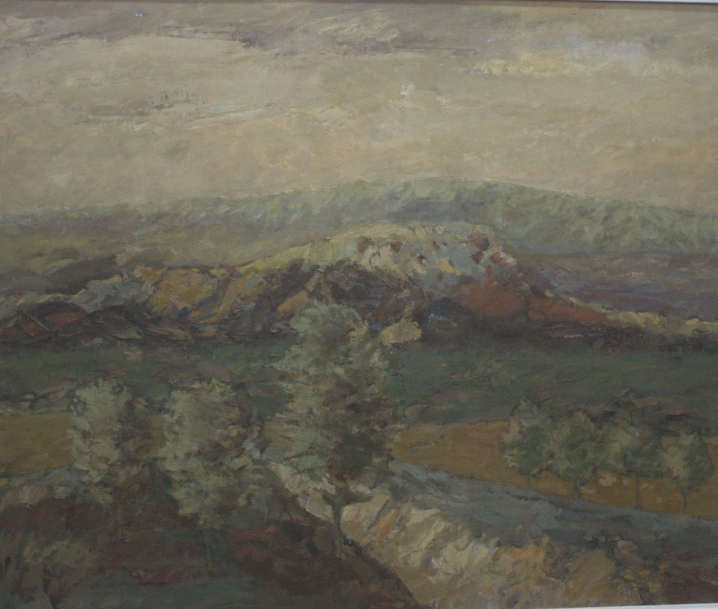 A hill of ochre and reddish rock above a green meadow, with small trees under a beige sky.